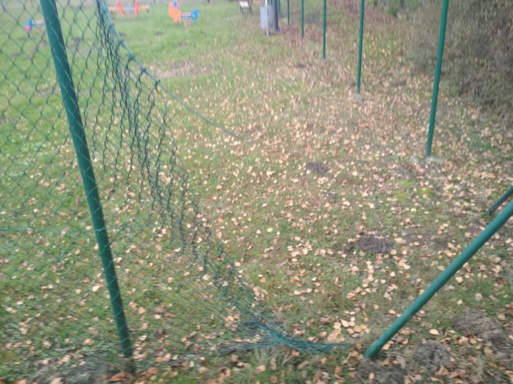 Zdjęcie uszkodzonego ogrodzenia przy placu zabaw. 